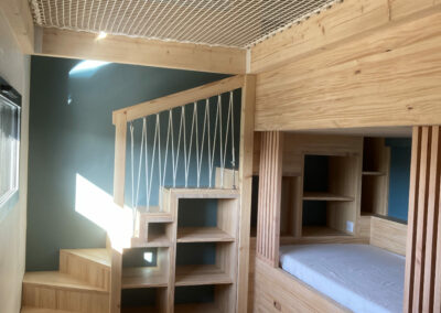Vue d'ensemble du bas de la chambre enfant tout en bois, son lit à tiroirs, clairvoie pour protéger des chutes nocturnes, rangement sous l'escalier
