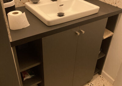 Meuble toilettes en mélaminé noir avec 2 portes et étagères ouvertes sur les côtés.